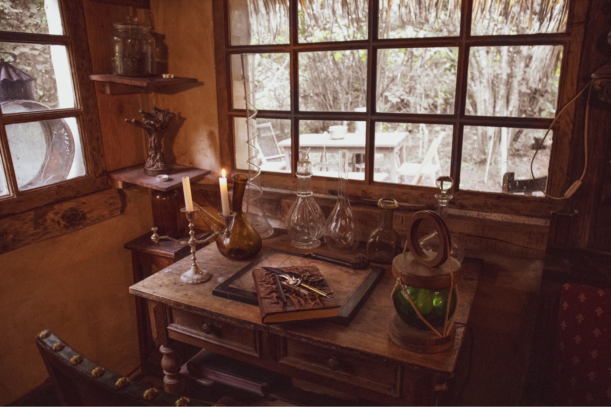 A cluttered table with candles, potion flasks, and a leatherbound tome. The window shows a snowy scene outside. This looks like a wizard's study.